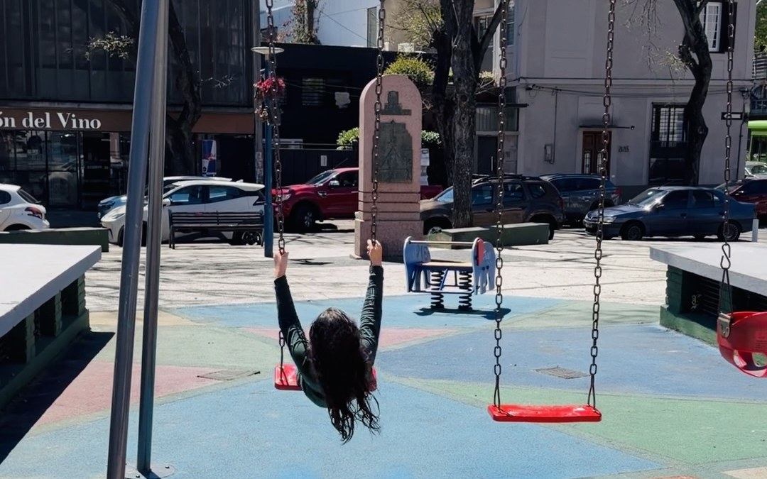Una nena se hamaca en la Placita Williman, con el monumento al fondo